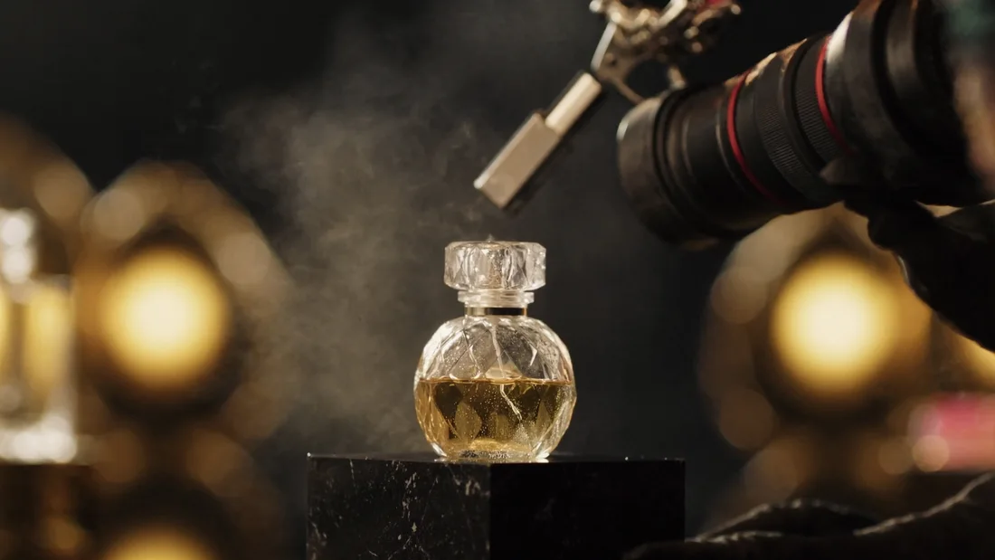 Fotografia macro de frasco de perfume de cristal sobre pedestal de pedra, com névoa e luz dourada